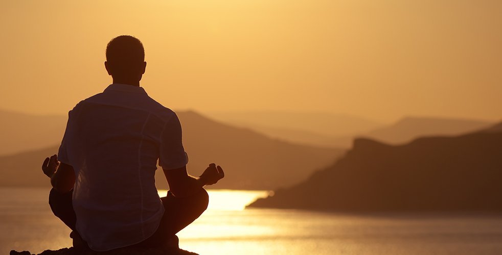 Man meditating at sunset in front of lake